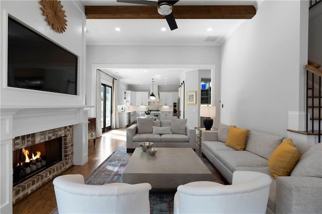 living room featuring ceiling fan, beamed ceiling, a lit fireplace, recessed lighting, and wood finished floors