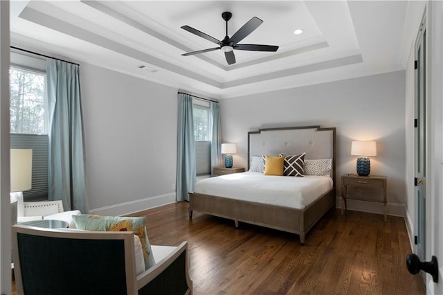 bedroom with a tray ceiling, multiple windows, wood finished floors, and baseboards