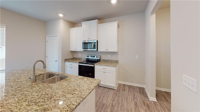 kitchen with light stone counters, light wood finished floors, appliances with stainless steel finishes, white cabinetry, and a sink