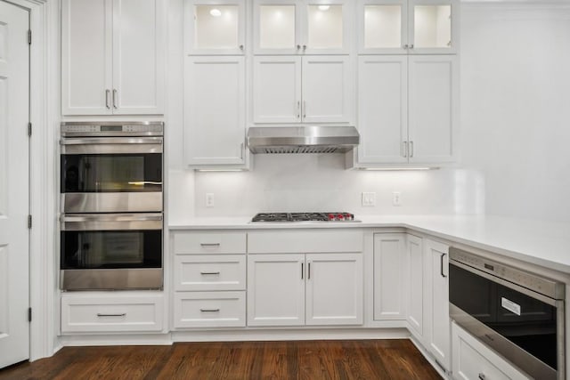 kitchen with appliances with stainless steel finishes, dark hardwood / wood-style floors, white cabinets, and range hood