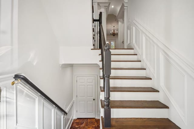 stairs with an inviting chandelier, a decorative wall, and wainscoting