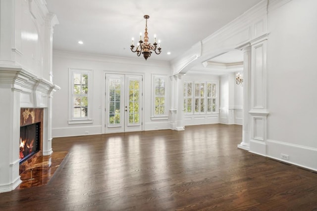 unfurnished living room featuring dark wood-type flooring, a notable chandelier, a high end fireplace, ornamental molding, and ornate columns