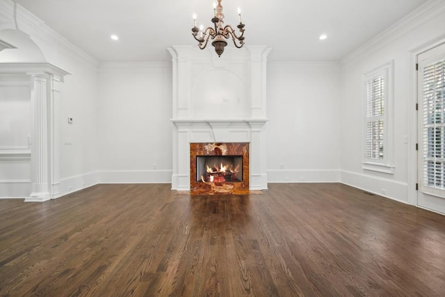 unfurnished living room featuring ornate columns, ornamental molding, dark hardwood / wood-style floors, a notable chandelier, and a tiled fireplace