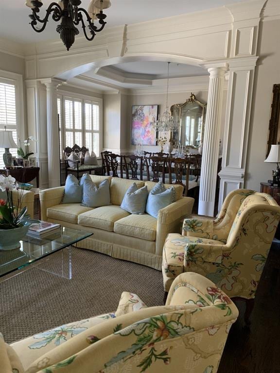 living room featuring a healthy amount of sunlight, ornamental molding, a chandelier, and decorative columns