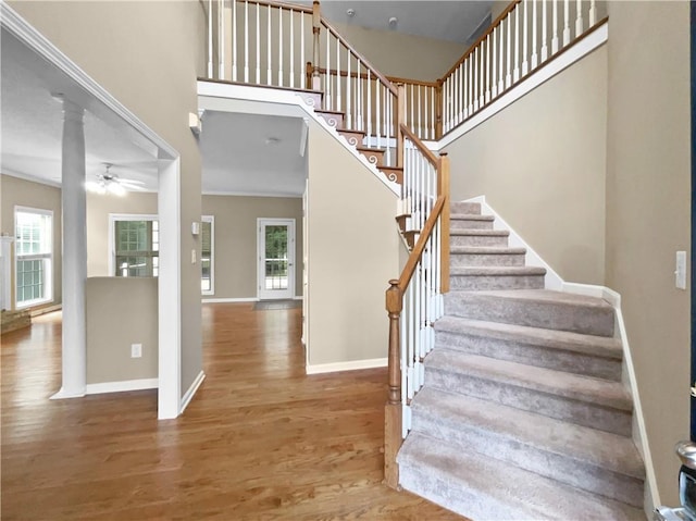 staircase featuring ornate columns, wood-type flooring, ornamental molding, and plenty of natural light