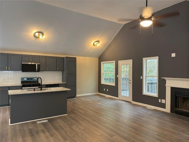 kitchen with dark wood-type flooring, sink, a kitchen island with sink, and light stone counters