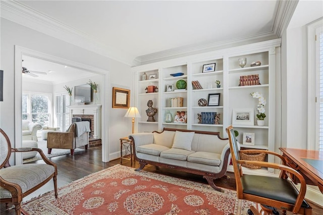 living area with a fireplace, wood finished floors, a ceiling fan, baseboards, and crown molding