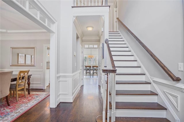 stairway with ornamental molding, wainscoting, wood finished floors, and a decorative wall