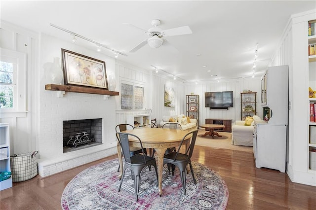 dining space with a brick fireplace, a decorative wall, track lighting, and wood finished floors