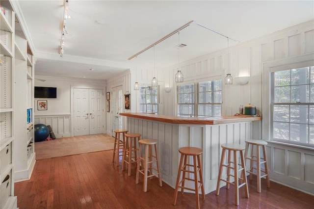 kitchen featuring hardwood / wood-style flooring, ornamental molding, a kitchen breakfast bar, rail lighting, and a decorative wall