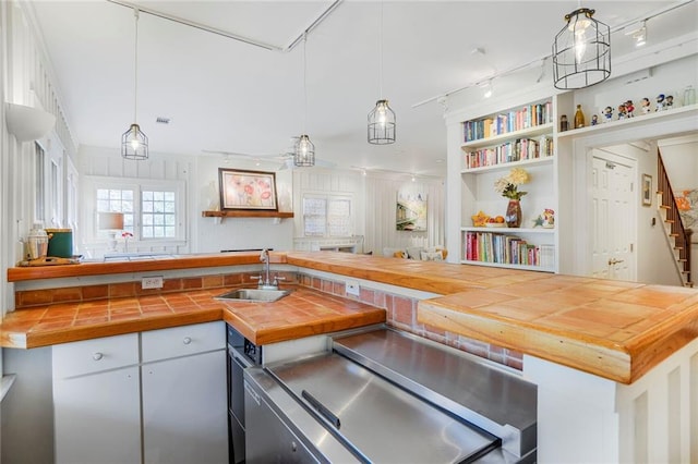 kitchen featuring built in shelves, decorative light fixtures, rail lighting, a sink, and wood counters