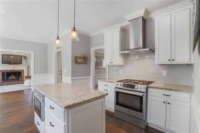 kitchen with a wainscoted wall, dark wood-type flooring, a brick fireplace, wall chimney range hood, and stainless steel gas range