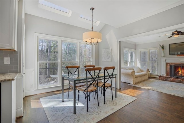 dining space featuring lofted ceiling with skylight, a fireplace, wood finished floors, and a wealth of natural light