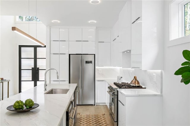 kitchen featuring sink, white cabinets, hanging light fixtures, light stone countertops, and premium appliances