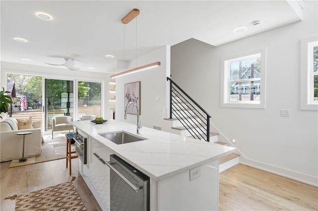 kitchen with dishwasher, an island with sink, light wood-type flooring, pendant lighting, and sink