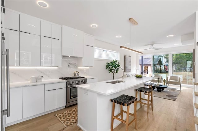 kitchen with a kitchen breakfast bar, high end range, a center island with sink, sink, and white cabinetry