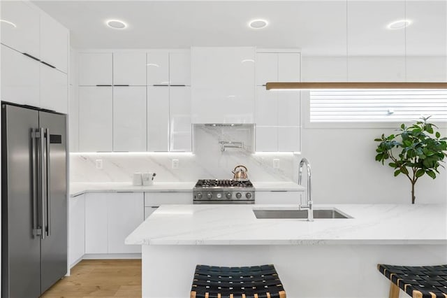 kitchen with light stone counters, white cabinets, high end refrigerator, stove, and sink