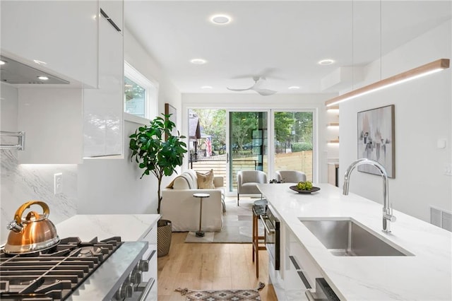 kitchen with sink, white cabinetry, light stone counters, light wood-type flooring, and ceiling fan