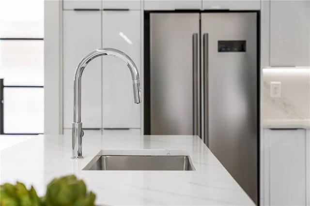 interior details featuring high end refrigerator, light stone countertops, sink, and white cabinetry