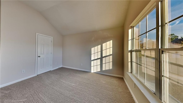 carpeted spare room featuring baseboards and vaulted ceiling