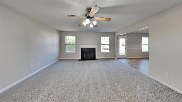 unfurnished living room featuring a fireplace with flush hearth, ceiling fan, baseboards, and carpet floors