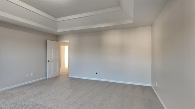 carpeted empty room featuring a tray ceiling and baseboards