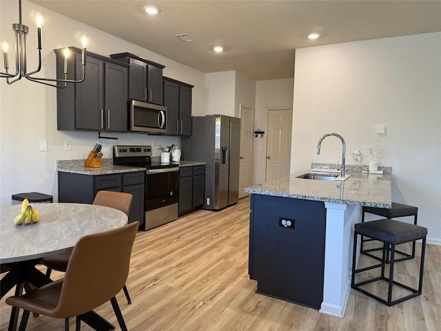 kitchen with light wood-type flooring, a peninsula, a breakfast bar area, appliances with stainless steel finishes, and a sink