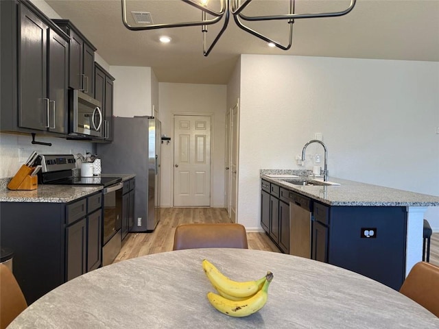 kitchen featuring light wood finished floors, a sink, light stone counters, and appliances with stainless steel finishes
