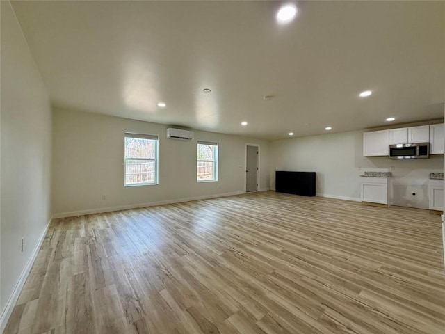 unfurnished living room with recessed lighting, light wood-type flooring, an AC wall unit, and baseboards