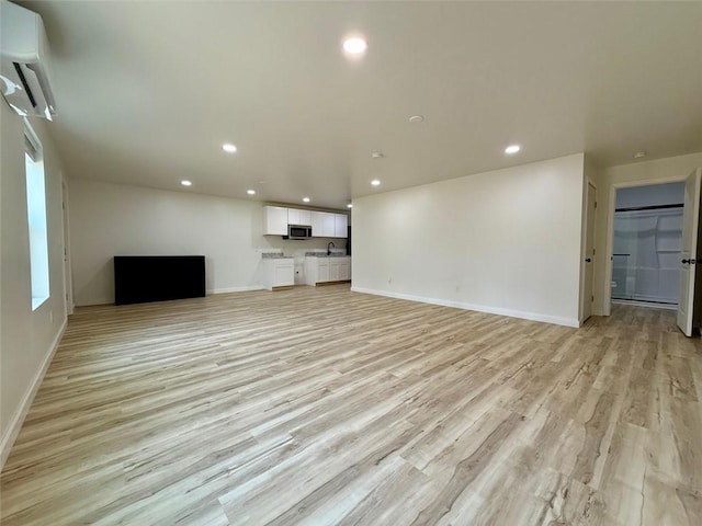 unfurnished living room with light wood finished floors, a wall mounted air conditioner, baseboards, and recessed lighting