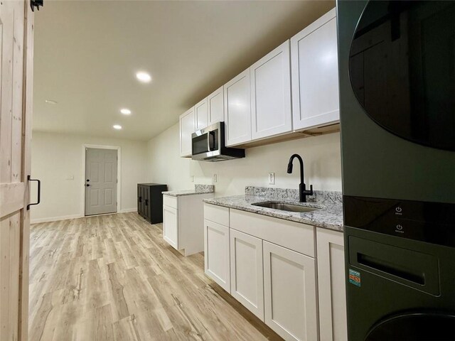 kitchen with light stone countertops, light wood-style flooring, stainless steel microwave, a sink, and stacked washer and clothes dryer