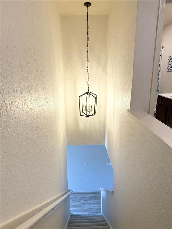 stairway featuring a chandelier, wood finished floors, and a textured wall
