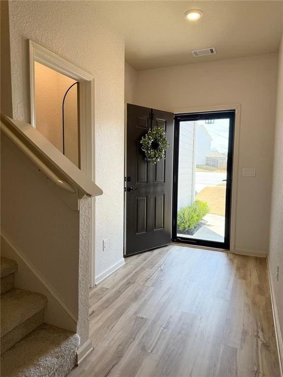 entrance foyer featuring visible vents, light wood-style flooring, stairway, and baseboards