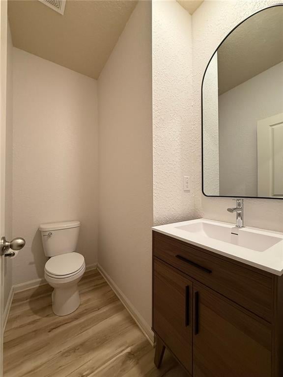 half bathroom with toilet, wood finished floors, vanity, and baseboards