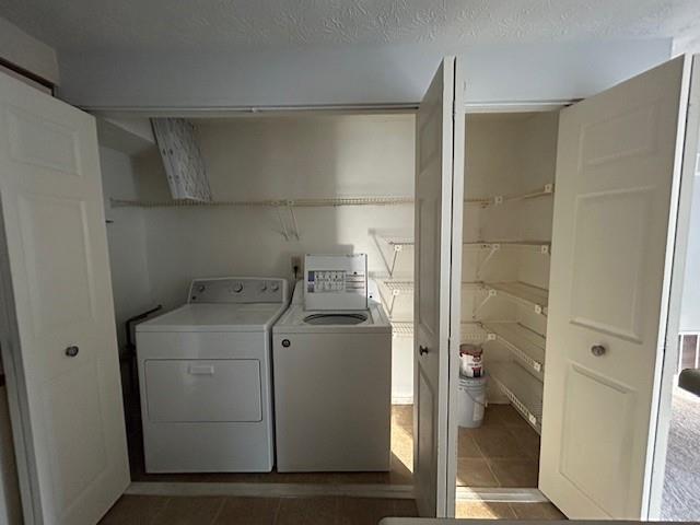 washroom with a textured ceiling, dark tile patterned floors, and washing machine and clothes dryer