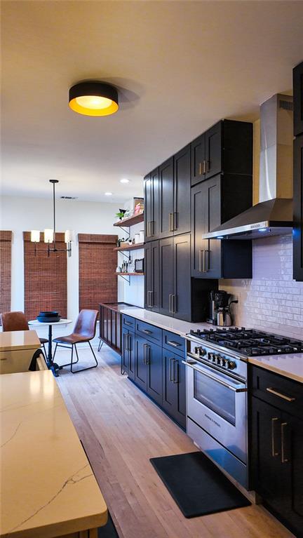 kitchen with light wood finished floors, decorative backsplash, wall chimney exhaust hood, and high end stainless steel range