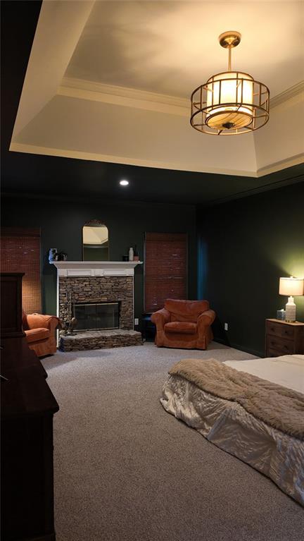 bedroom featuring a stone fireplace, ornamental molding, and carpet flooring