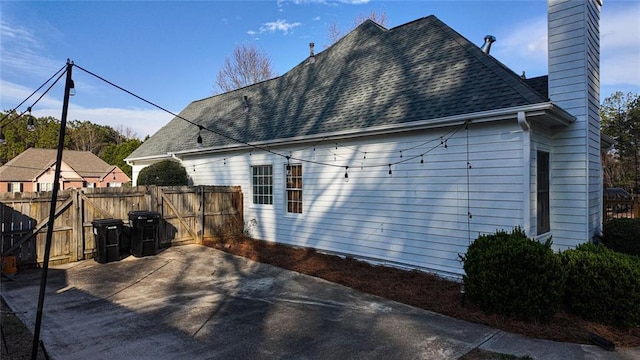 view of side of property featuring a patio, a chimney, roof with shingles, and fence