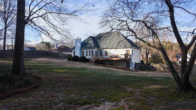 back of house featuring a chimney, a yard, a wooden deck, and a fenced backyard