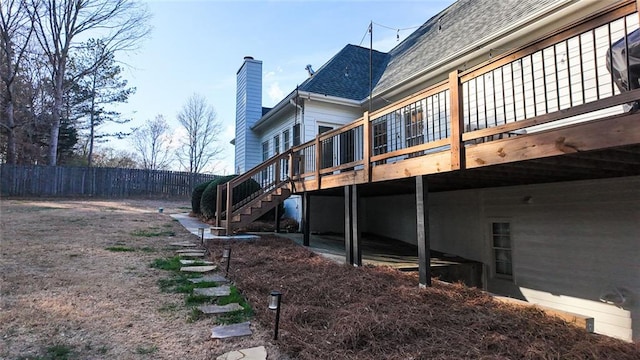 view of side of property with stairway, fence, roof with shingles, a chimney, and a deck