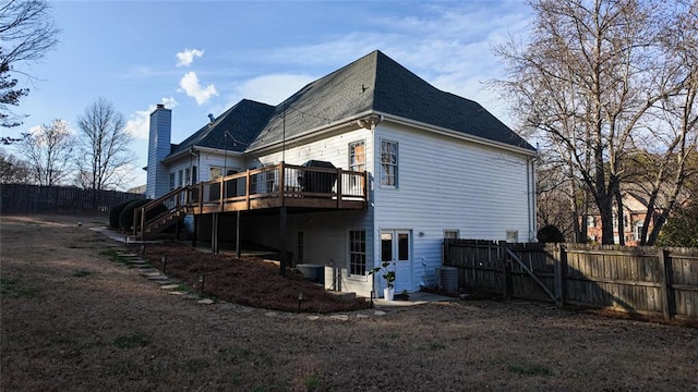 rear view of house featuring a deck, stairs, fence, and a chimney