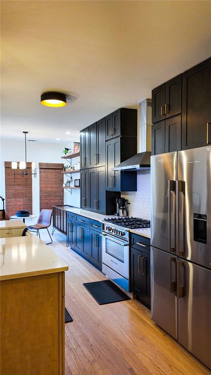 kitchen with light wood finished floors, tasteful backsplash, light countertops, stainless steel appliances, and wall chimney exhaust hood