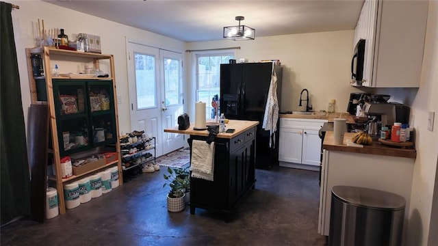 kitchen featuring black appliances, a sink, finished concrete flooring, white cabinets, and hanging light fixtures