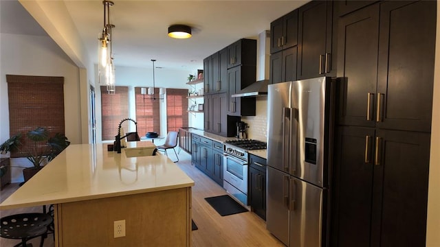 kitchen featuring a kitchen island with sink, a sink, appliances with stainless steel finishes, wall chimney exhaust hood, and light countertops