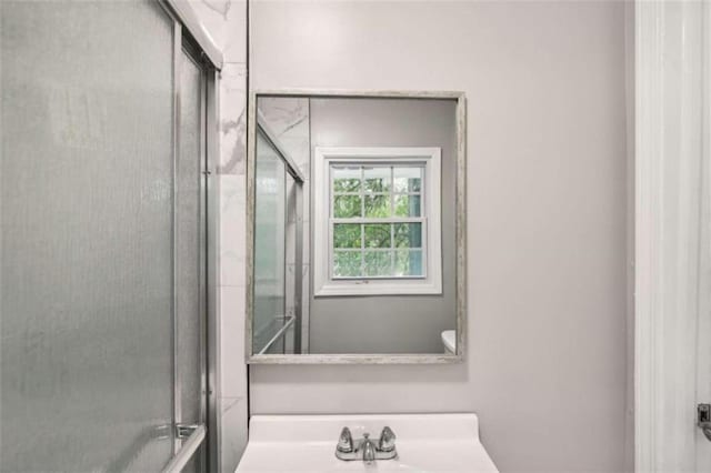 bathroom featuring a shower with door and sink