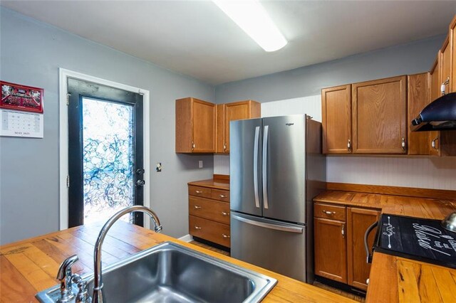 kitchen featuring freestanding refrigerator, a sink, brown cabinetry, and butcher block counters