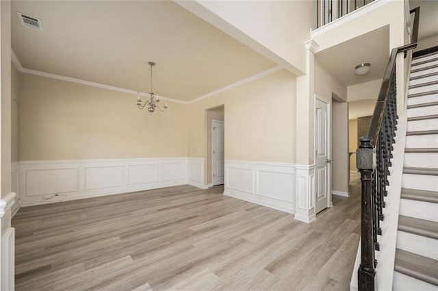 empty room featuring a chandelier, ornamental molding, and light wood-type flooring