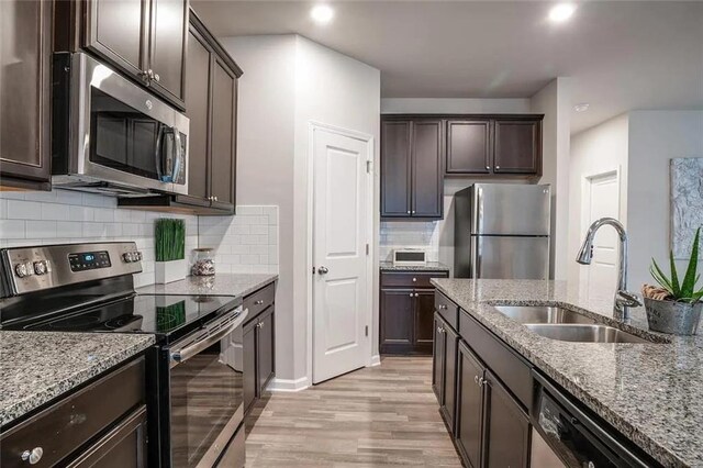 kitchen with dark brown cabinetry, light stone countertops, appliances with stainless steel finishes, and a sink