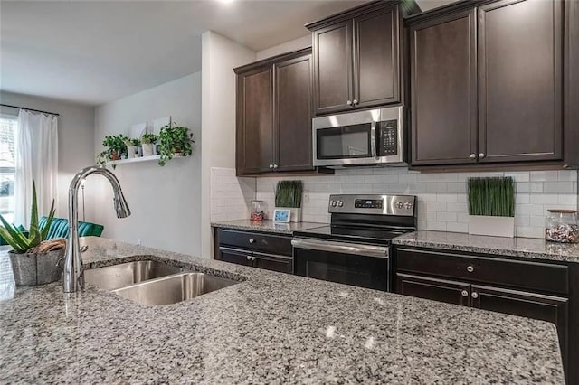 kitchen with a sink, light stone counters, tasteful backsplash, stainless steel appliances, and dark brown cabinets