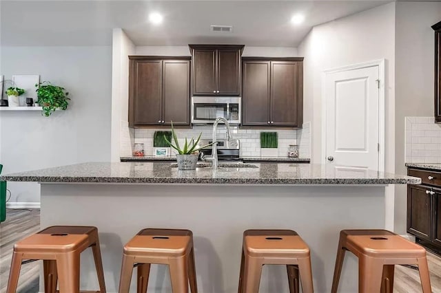 kitchen with stainless steel microwave, a kitchen bar, and dark brown cabinets